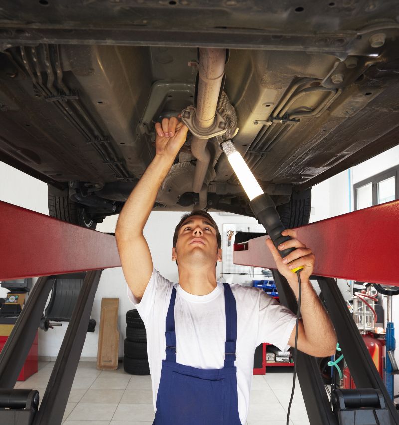 Mechanic standing under car engine and holding a lamp - MOT Testing Glenrothes, Fife